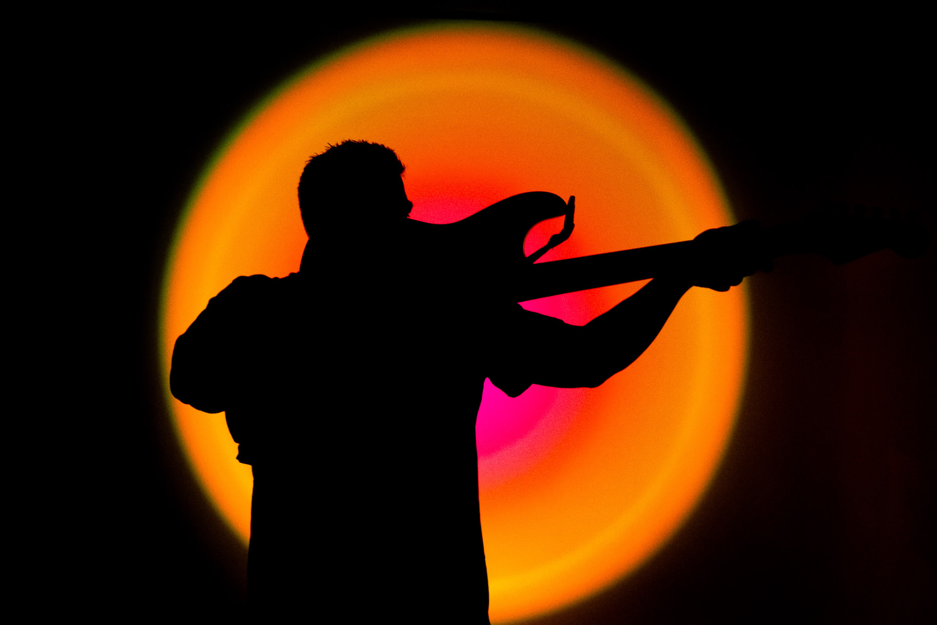 Silhouette of a guitarist in front of an orange and pink backlight