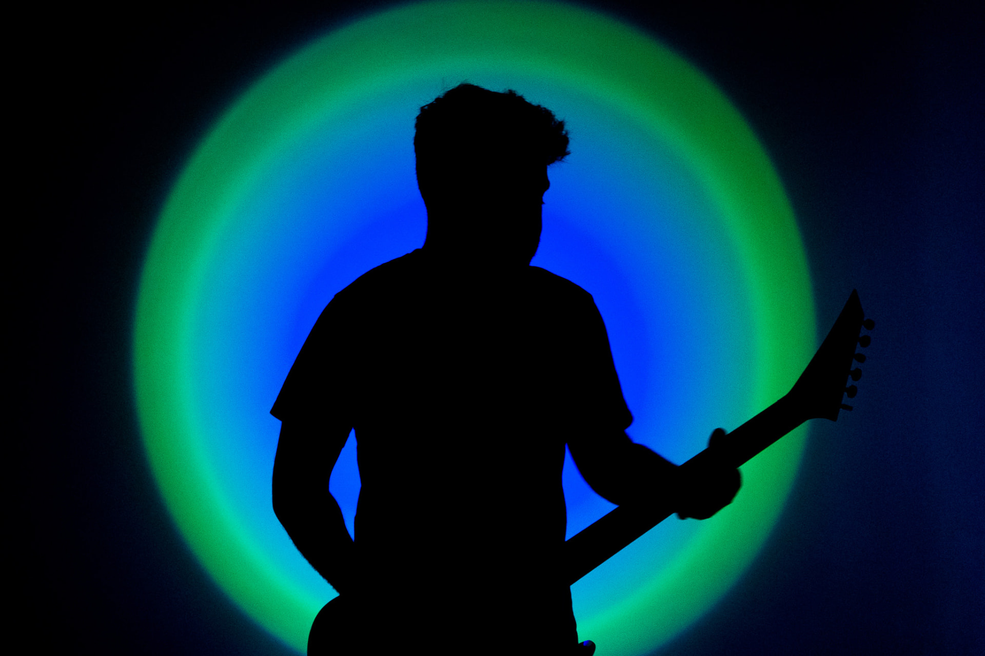 Silhouette of a guitarist in front of a blue and green backlight